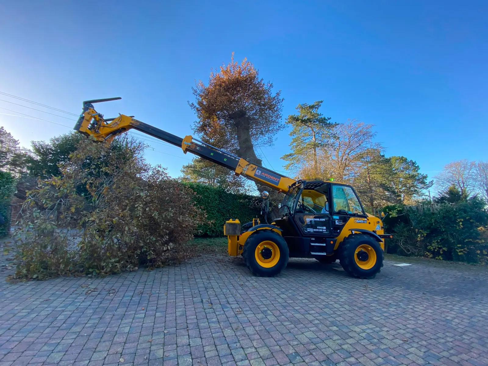 Telehandler lifting a sectioned tree trunk clear of a driveway during a tree removal